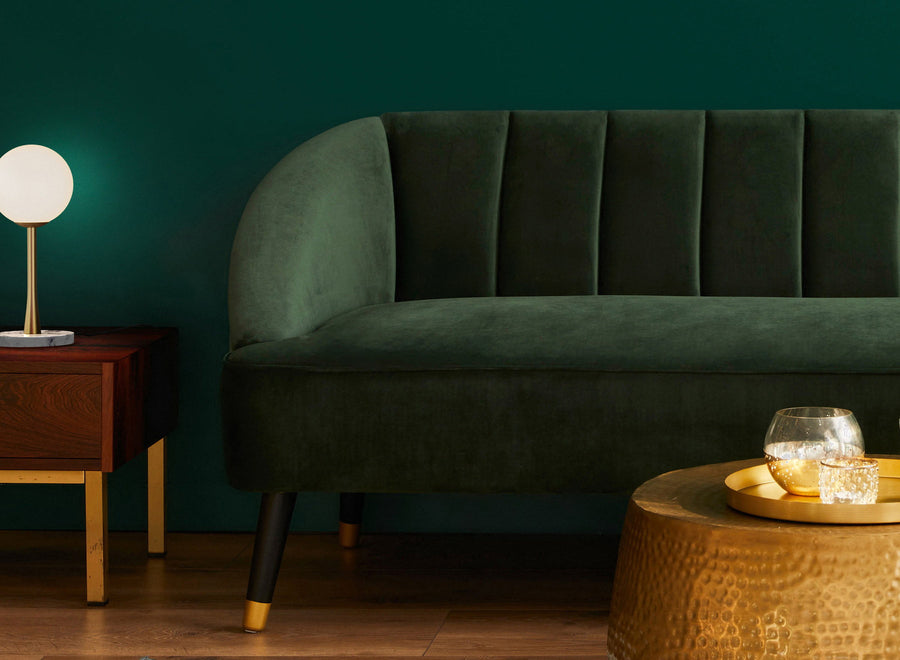 Maximalist living room with emerald green velvet sofa, matching wall and hammered brass pouf