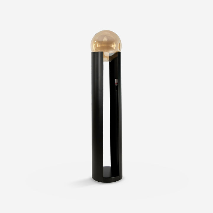 Lámpara pie cristal fumé ámbar y acero negro sobre fondo gris de estudio