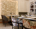 Restaurant dining room with laid tables, upholstered chairs and a lit stone wall